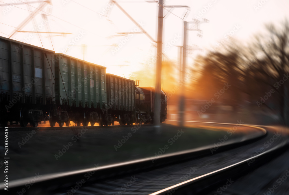 Freight train passing turn at sunset. Train carrying cargo under the rays of the setting sun.Motion blur. Freight train passing turn at sunset. Train carrying cargo under the rays of the setting sun.Motion blur.