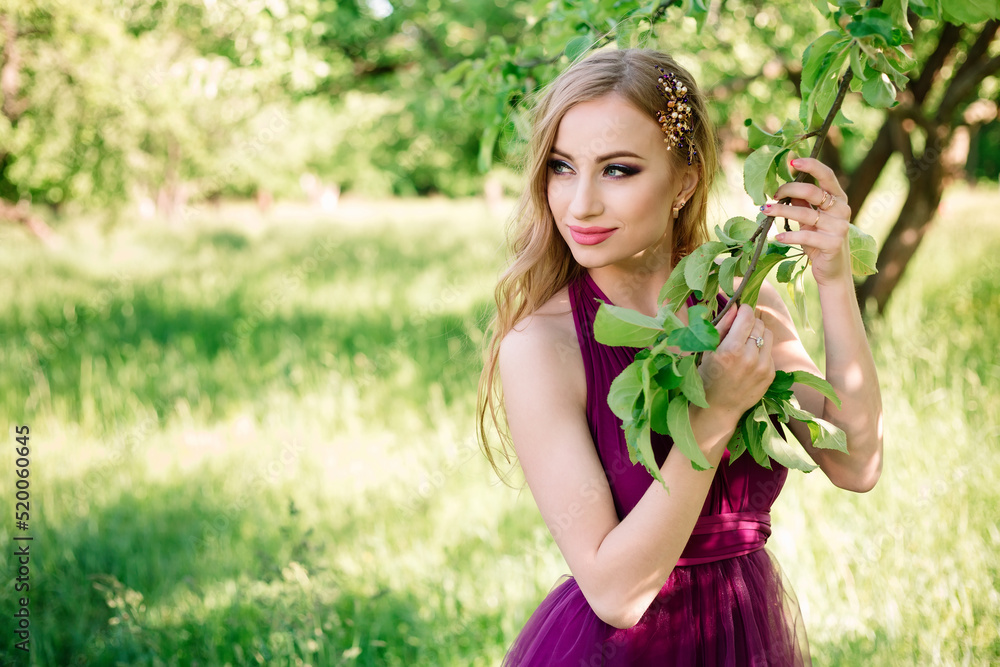 Professional model with makeup and hairstyle poses in a green garden and holds an apple tree branch in a fashionable dress. Beauty shot and copy space. Professional model with makeup and hairstyle poses in a green garden and holds an apple tree branch in a fashionable dress. Beauty shot and copy space.