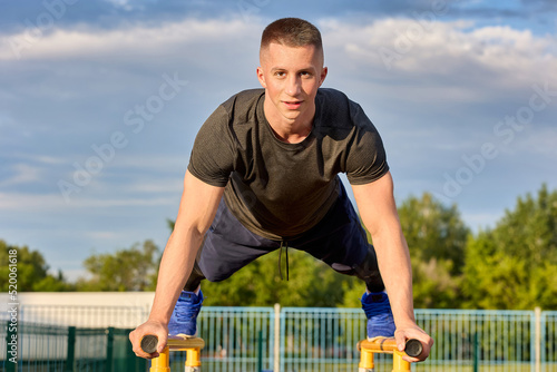 Strong gymnast stands in a bar on parallel bars during training. Caucasian athlete performs gymnastic exercises on parallel bars in the open air photo