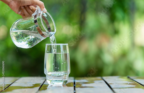 Pour clean water from a jug into a glass placed on a wooden bar.	
