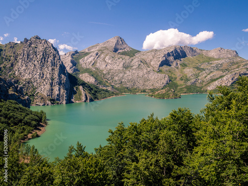 Paisaje de montaña con un lago alpino rodeado de bosques y montañas rocosas con un cielo azul de nubes blancas. photo