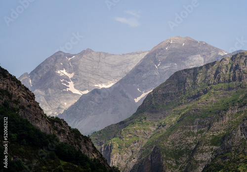 Valle alpino con montañas de color gris con nieve de fondo y cielo azul