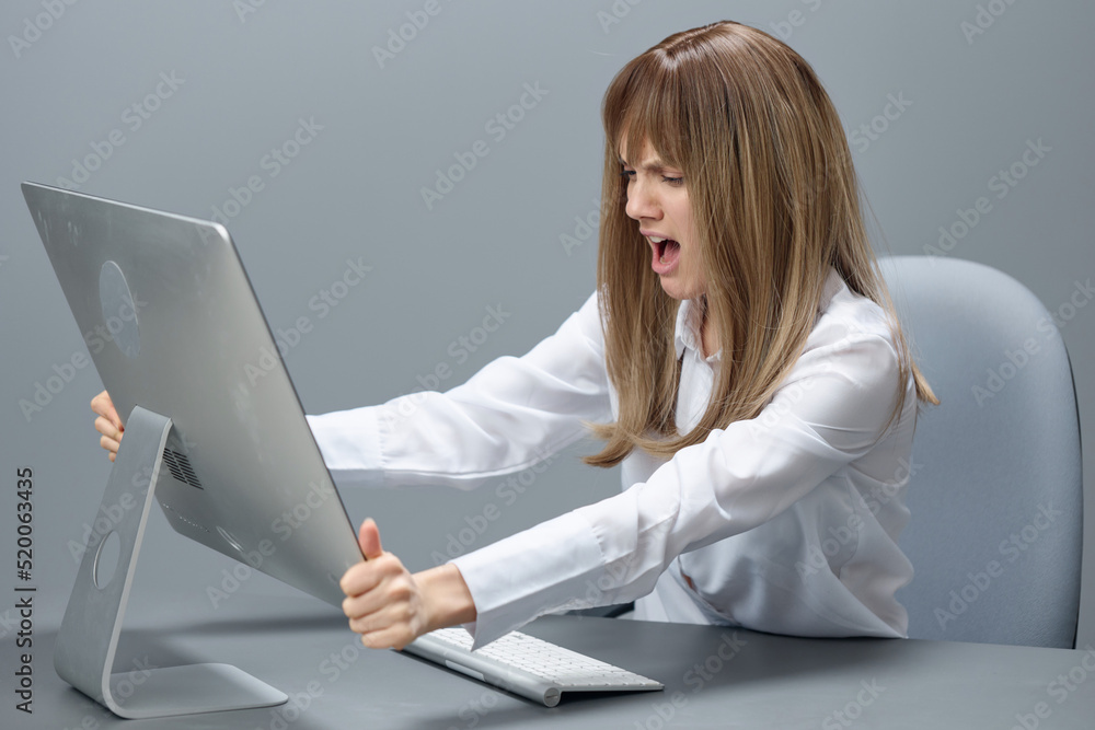 Angry evil pretty blonde businesswoman screaming to desktop Raging after computer software crash error sitting at workplace in gray modern office. Technology And Operation Problem Concept. Copy space Angry evil pretty blonde businesswoman screaming to desktop Raging after computer software crash error sitting at workplace in gray modern office. Technology And Operation Problem Concept. Copy space