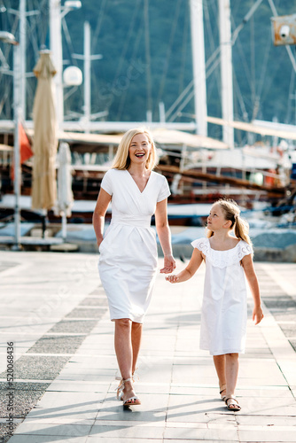 Smiling caucasian blonde  mother and daugher walking by harbor with yachts on a touristic sea resort © linortis