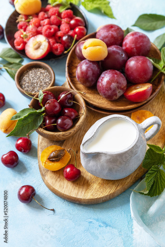 Ingredients for a healthy smoothie. Milk and berries (raspberry, cherry, plum, apricot) on a stone tabletop. Healthy eating, raw food diet and vegan food concept. Copy space.