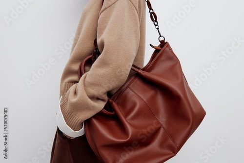 a gentle beautiful woman is standing sideways on a light background in a sweater and shirt, wearing a bag on one shoulder, brought it back a little and put her hand in her pocket, The subject is close