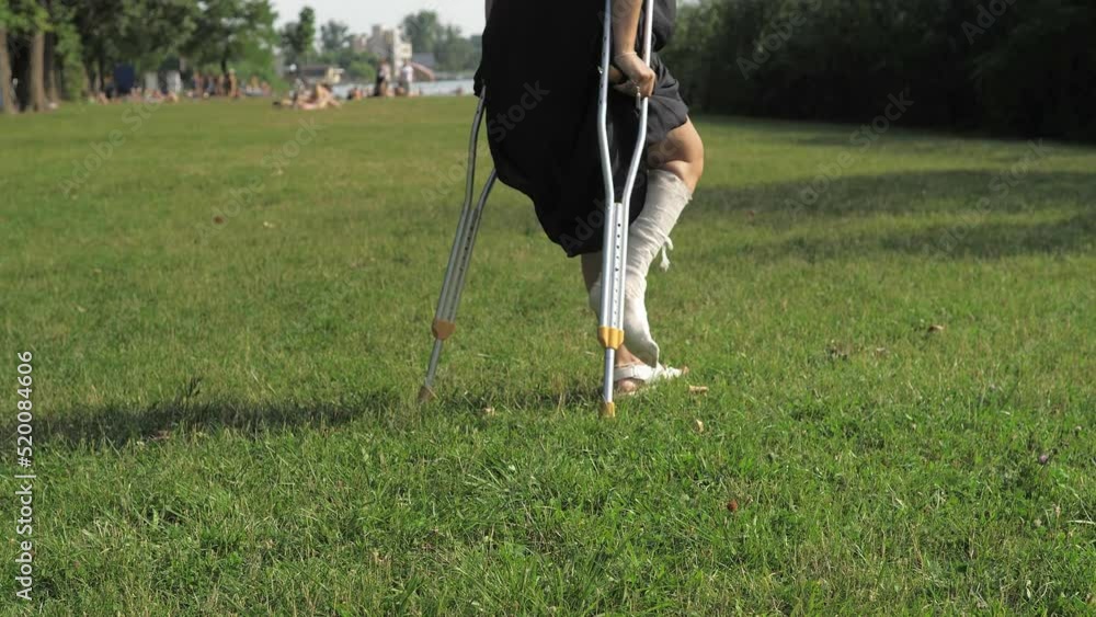 Stockvideo A young girl with a cast walks around the park on crutches