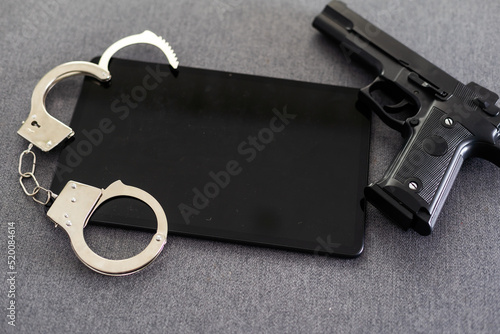 Gun, smartphone with handcuffs over dark background