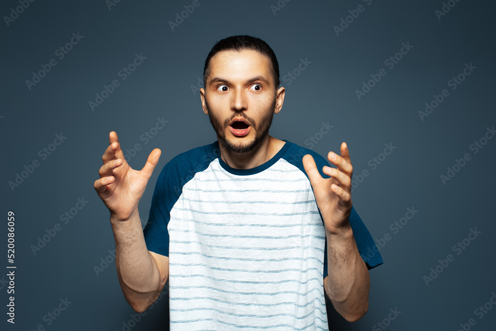 Fototapeta premium Studio portrait of shocked guy in shirt, on blue background.
