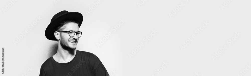 Panoramic banner portrait of young smiling man looking away  on white background with copy space. Black and white photo.