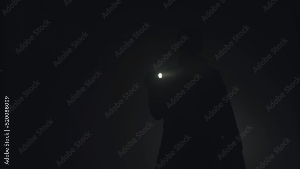Silhouette of man shining with flashlight in the dark. Stock footage. Silhouette of man in thick fog