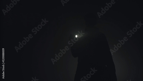 Silhouette of man shining with flashlight in the dark. Stock footage. Silhouette of man in thick fog