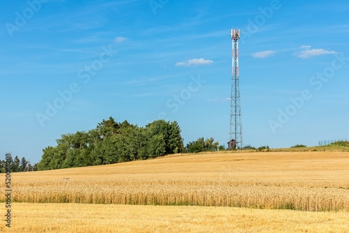 Iron communications tower on the hill with wheat field. Agriculture. Growing wheat. Grain trading. New GSM antennas on a high tower against a blue sky.