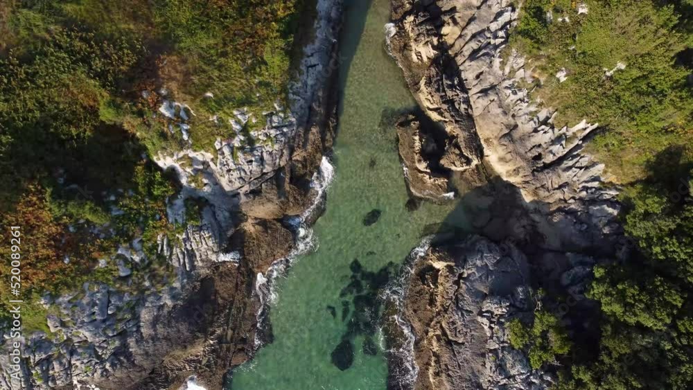 drone aerial view of the Cantabrian coast with the rough sea and the waves crashing against the rocks on a sunny day with the village in the background. drone aerial view of the Cantabrian coast with the rough sea and the waves crashing against the rocks on a sunny day with the village in the background.