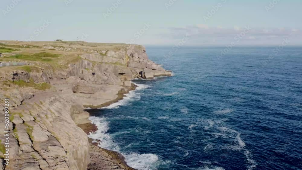drone aerial view of the Cantabrian coast with the rough sea and the waves crashing against the rocks on a sunny day with the village in the background. drone aerial view of the Cantabrian coast with the rough sea and the waves crashing against the rocks on a sunny day with the village in the background.