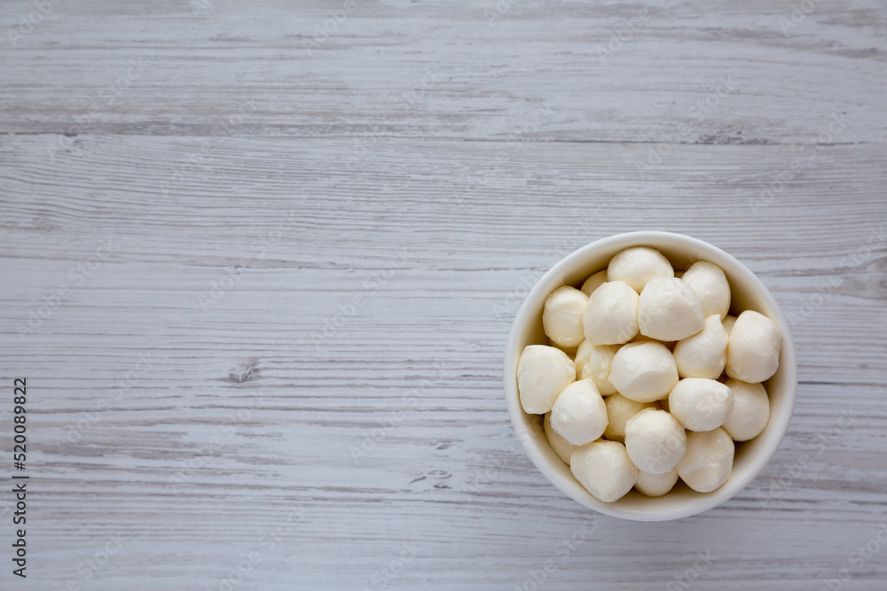 Homemade organic mozzarella cheese in a bowl on a white wooden background, top view. Flat lay, overhead, from above. Space for text. Homemade organic mozzarella cheese in a bowl on a white wooden background, top view. Flat lay, overhead, from above. Space for text.