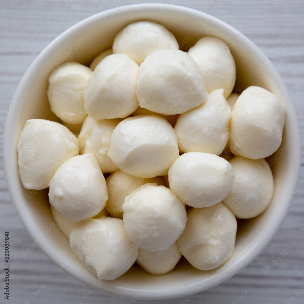 Homemade organic mozzarella cheese in a bowl on a white wooden background, top view. Flat lay, overhead, from above. Close-up. Homemade organic mozzarella cheese in a bowl on a white wooden background, top view. Flat lay, overhead, from above. Close-up.