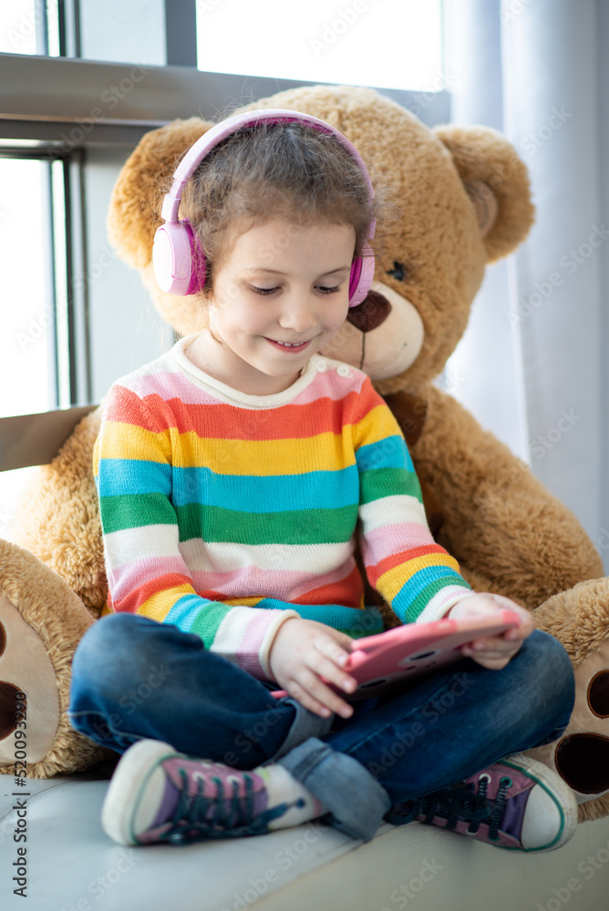 Cute little girl holding tablet computer in her hands. She is in headphones. Cute little girl holding tablet computer in her hands. She is in headphones.