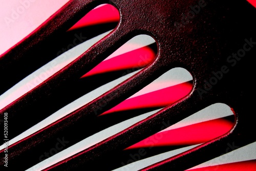 Espumadera de teflòn negro con ranuras incide la luz roja a travès de ellas formando diseños mitad rojo y blanco, presenta una ilustraciòn original abstracta para fondos  photo
