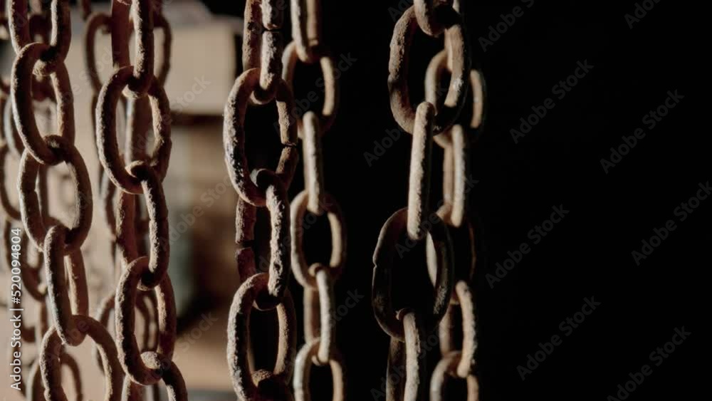 Rusty metal old chain dangling in dark indoor space. Close up of the links of an aged iron chain covered with corrosion and dust. Rough damaged metal structure. Grunge. Strong uneven metal connections Rusty metal old chain dangling in dark indoor space. Close up of the links of an aged iron chain covered with corrosion and dust. Rough damaged metal structure. Grunge. Strong uneven metal connections