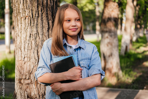 Shying girl holding notebooks looking away outdoor. Child feels awkward. Back to school concept
