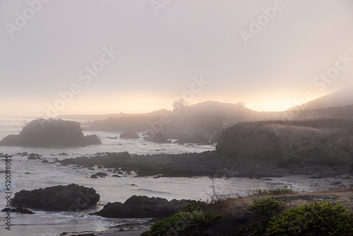 Moody coastal fog at sunset on the rugged pacific coast near Cayucos, California. Looking down the coastline with rocky cliffs jutting out into the ocean. 