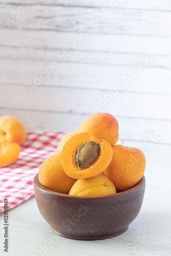 apricots in a wooden bowl on a white wooden background, apricot cut in half, red checkered towel, fresh fruit