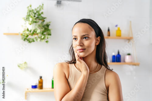 Beautiful hispanic brunette portrait against white tiled wall with cosmetics. Wellness and natural cosmetics