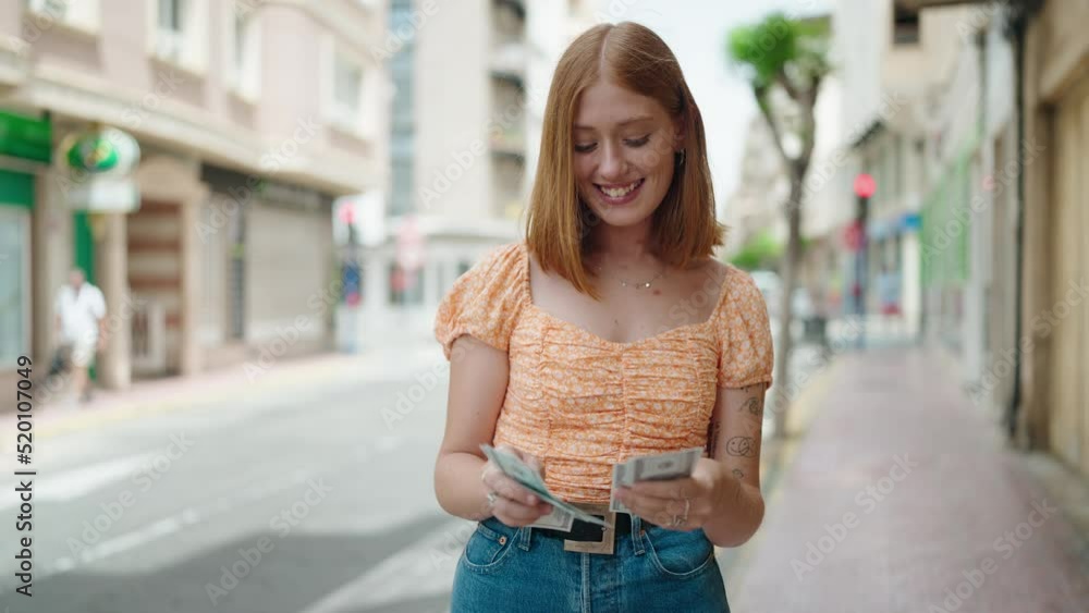 Young redhead woman smiling confident counting dollars at street Young redhead woman smiling confident counting dollars at street