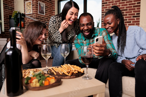 Photography Diverse group of friends at wine party celebrating birthday while watching funny clips on smartphone