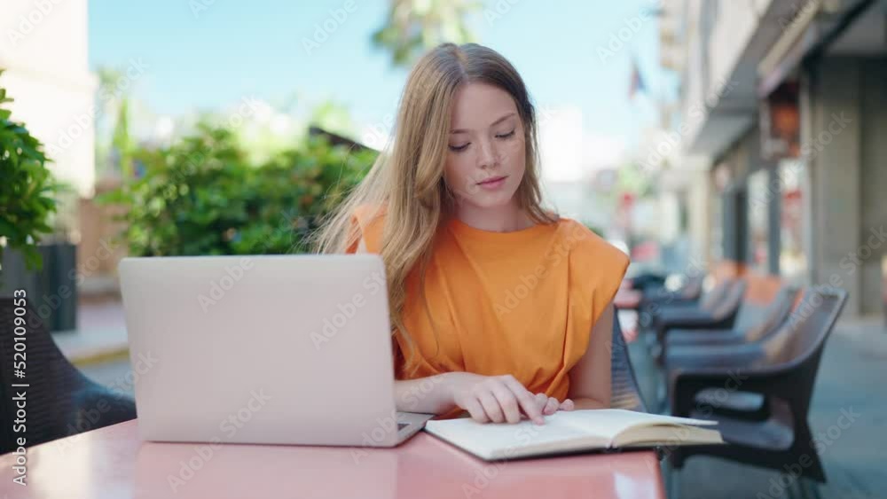 Young woman sitting on table studying at coffee shop terrace Young woman sitting on table studying at coffee shop terrace