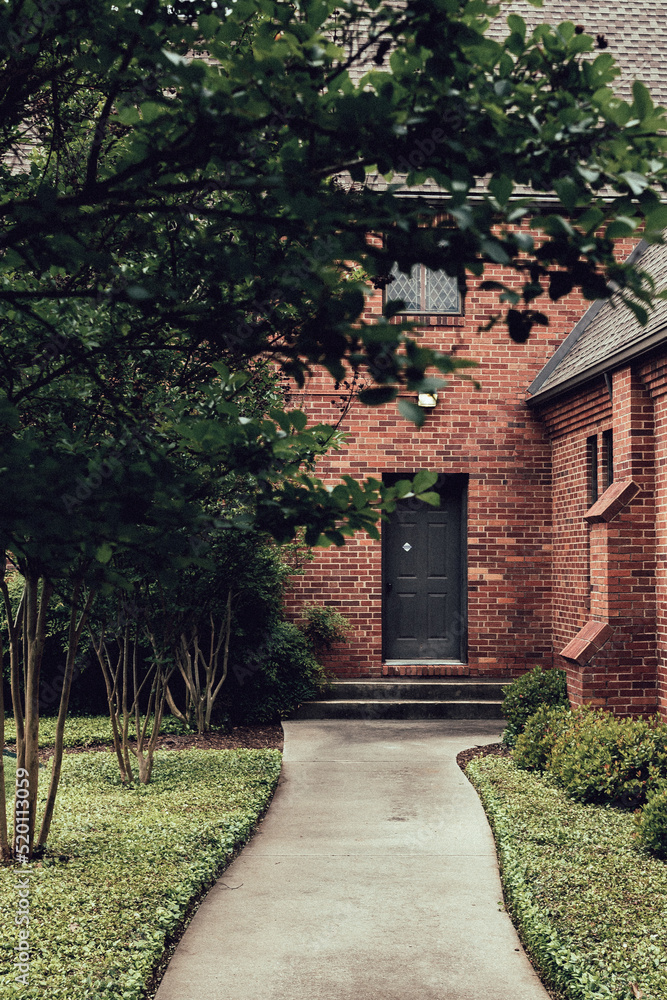 Tree-covered path leading to a church entrance with a black door.