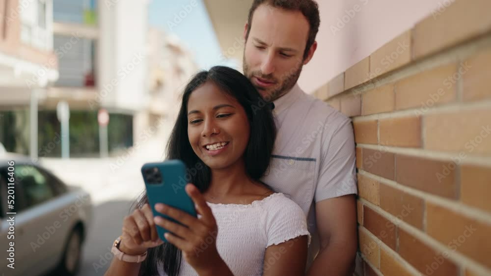 Man and woman interracial couple hugging each other using smartphone at street Man and woman interracial couple hugging each other using smartphone at street