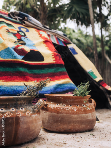 Ceramic jar with medicinal plants infusion in front of traditional Maya sauna covered with Mexican colorful carpets in the tropical forest of Tulum during sacred ceremony photo