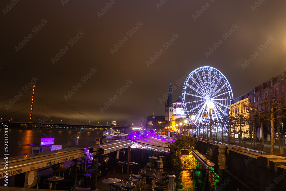 city bridge at night with fortune wheel carnival and church in europe market