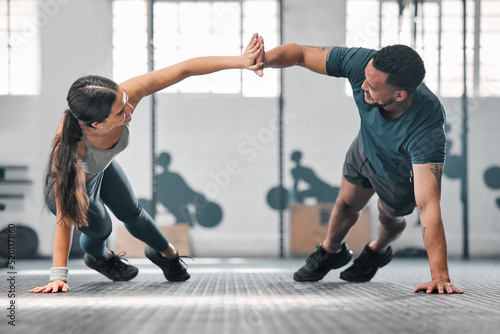 Healthy, fit and active gym partners exercising together as a couple, doing pushups and a high five. Boyfriend and girlfriend training and exercising in a health club as part of their workout routine