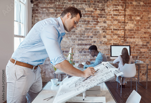 Architect, design engineer or building contractor drawing a plan on a drafting table for a project or development in his office. A male designer doing a blueprint sketch at an architecture company photo
