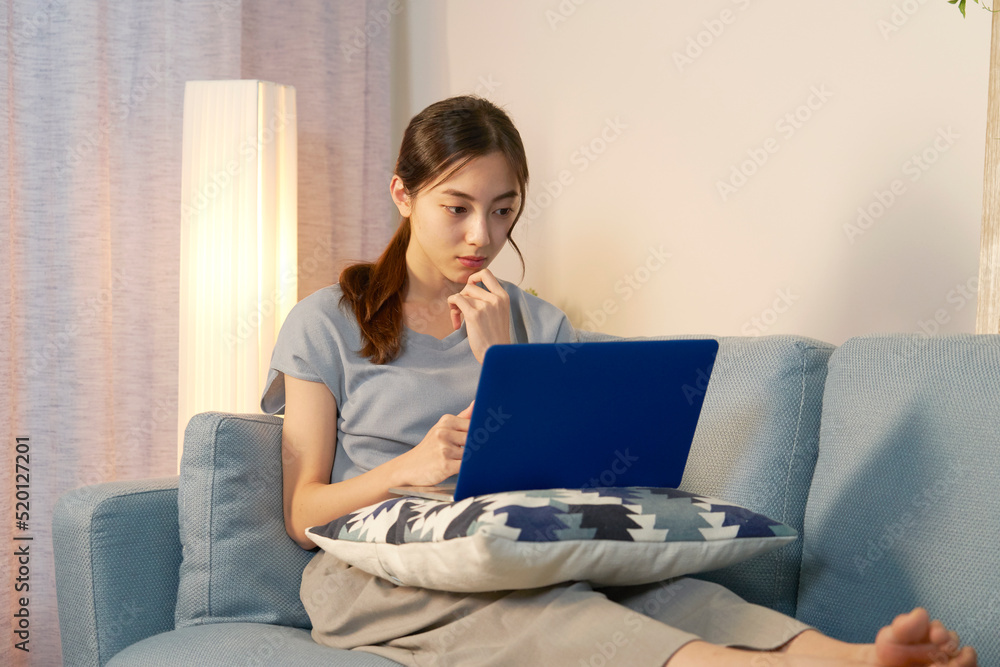 夜にリビングでパソコンを見て考える女性 夜にリビングでパソコンを見て考える女性