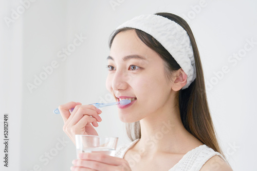 洗面室でコップを持って歯磨きする女性