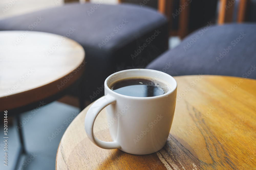 Closeup image of a white cup of hot coffee on wooden table in cafe Closeup image of a white cup of hot coffee on wooden table in cafe