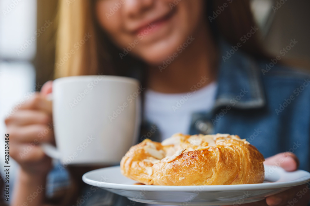 Closeup image of a young woman drinking coffee and eating a fresh almond croissant Closeup image of a young woman drinking coffee and eating a fresh almond croissant