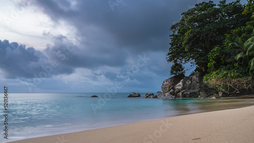 Beautiful tropical beach. Calm turquoise ocean and clean sand. Picturesque boulders and green vegetation at the water's edge. Clouds in the sky. Seychelles. Mahe Island. Beau Vallon Beach