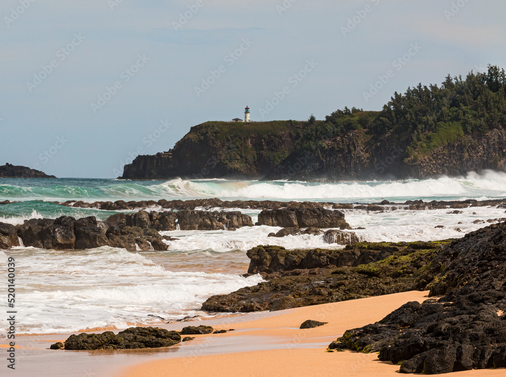 Waves Crash Over Exposed Coral Reef With Kilauea Lighthouse in The Distance, Kauapea Beach, Kauai, Hawaii, USA Waves Crash Over Exposed Coral Reef With Kilauea Lighthouse in The Distance, Kauapea Beach, Kauai, Hawaii, USA