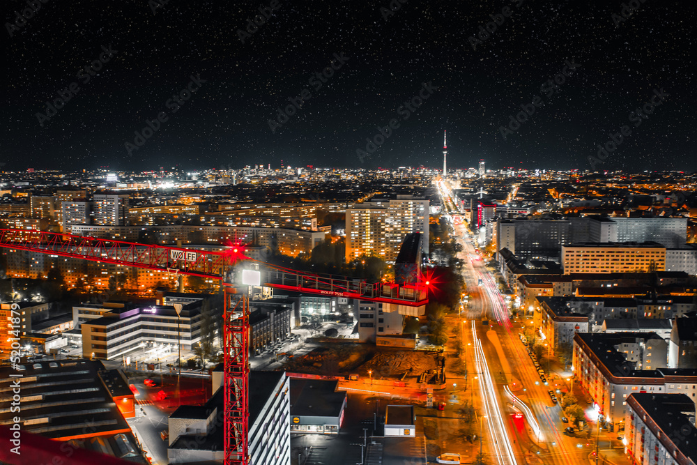 Obraz premium night shot of a crane and urban city with bright lights with long exposure traffic and car lights - berlin by night with the tv tower in the background