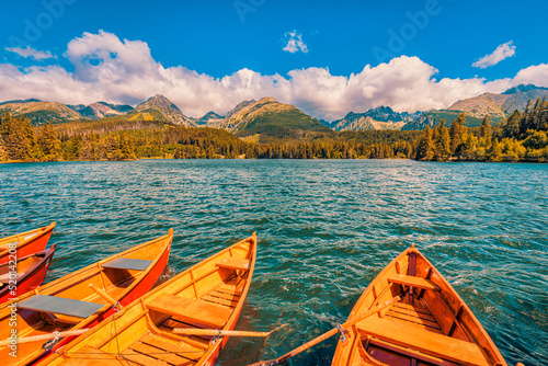 Fantastic mountain lake in National Park High Tatra Europe. Dramatic nature scenic. Beauty world. Wooden boats autumn landscape, beautiful sunny sky clouds relaxing water surface colorful forest trees
