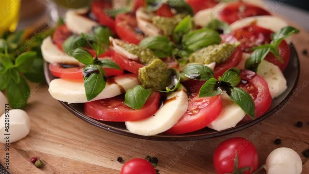 pouring pesto sauce on caprese salad with cherry tomatoes and mozzarella cheese balls pouring pesto sauce on caprese salad with cherry tomatoes and mozzarella cheese balls