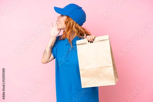 Young caucasian woman taking a bag of takeaway food isolated on pink background shouting with mouth wide open to the side