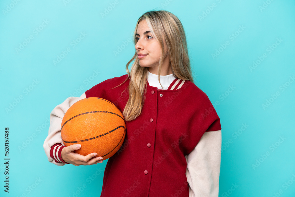 Young caucasian basketball player woman isolated on blue background looking to the side Young caucasian basketball player woman isolated on blue background looking to the side