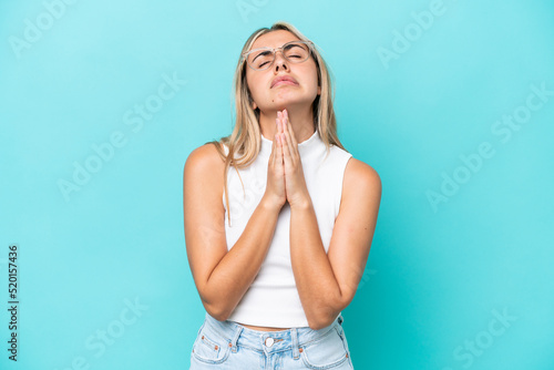 Young caucasian woman isolated on blue background keeps palm together. Person asks for something