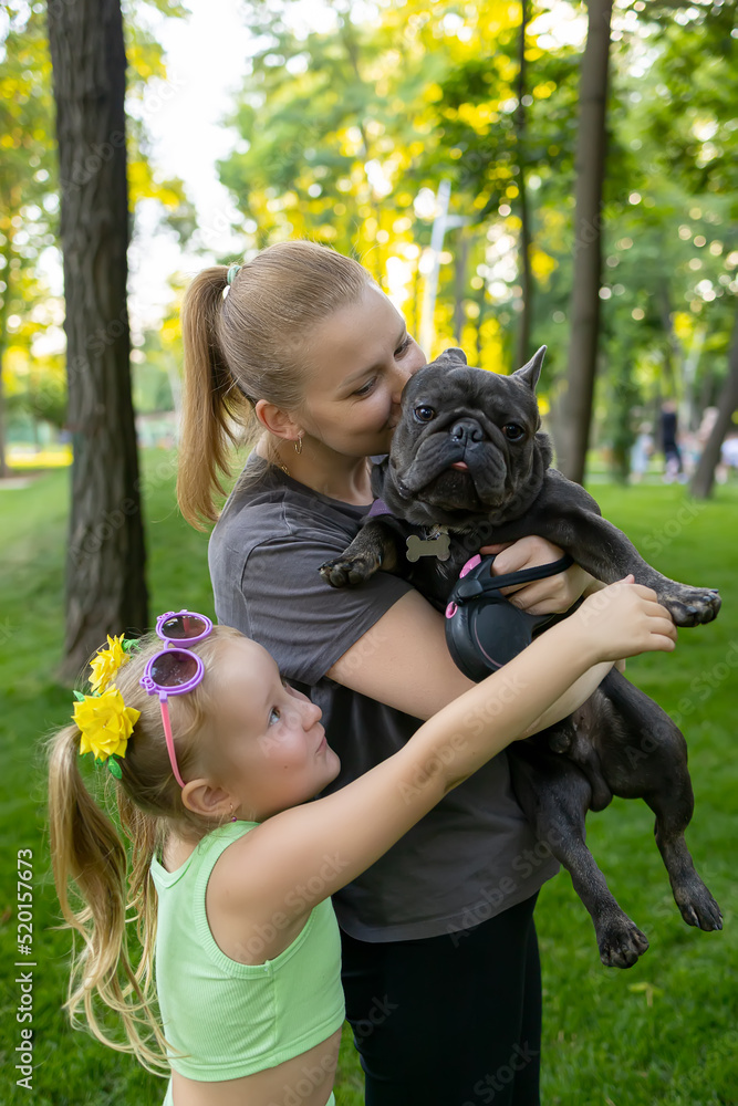 mother and daughter in the park hugging a french bulldog dog mother and daughter in the park hugging a french bulldog dog